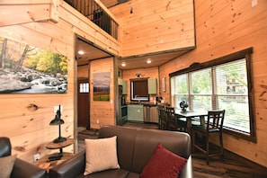 Ein Blockhaus-Interieur mit Essbereich, Küche und einem Wohnzimmer mit Sofa und einem Bild eines Wasserfalls.