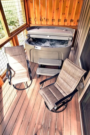 Una terraza de madera con un jacuzzi, dos sillas y una mesita.