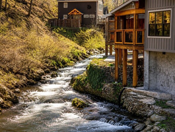 Una cabaña de madera con cimientos de piedra, un muelle de madera y un río que corre a su lado.