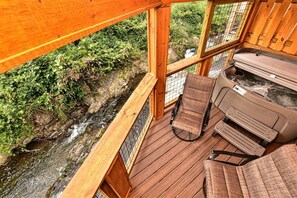 Une terrasse en bois avec un banc et un jacuzzi donnant sur un ruisseau.