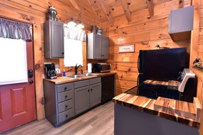 Una cocina compacta con paredes de madera, una puerta roja, armarios grises, una estufa negra y un microondas.