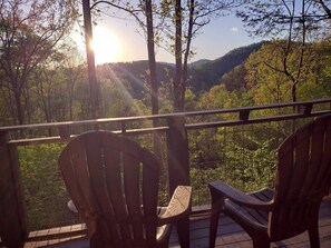 A deck with two Adirondack chairs overlooking a forested valley with a view of distant hills.
