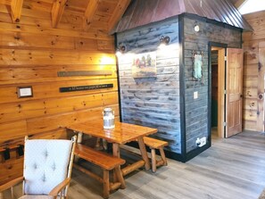 A wooden cabin interior with a dining table, benches, and a small kitchen area.