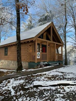 A wooden cabin with a porch, surrounded by trees and covered in snow.