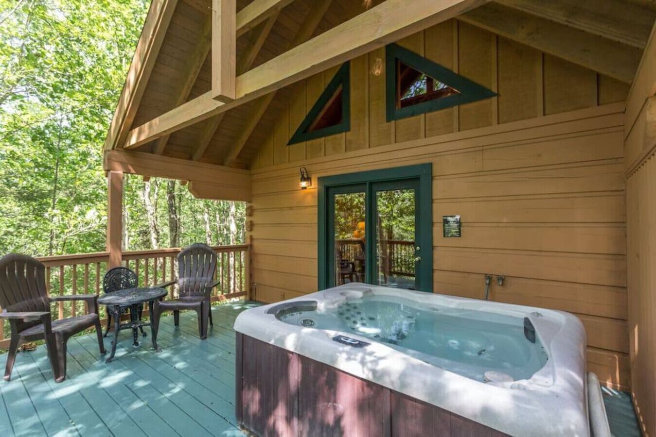 A wooden cabin with a hot tub, deck chairs, and a covered porch.