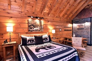 Acogedora habitación de cabaña de madera con una cama, dos mesitas de noche, una silla y un cuadro en la pared.