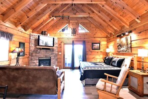 Acogedora habitación tipo cabaña de madera con chimenea, una cama, un sofá y un televisor.