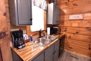 A compact kitchen with wooden walls, a double sink, a coffee maker, and a small refrigerator.