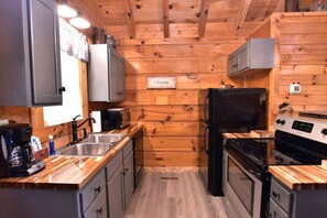 A compact kitchen with wooden walls, a stove, a sink, and cabinets.