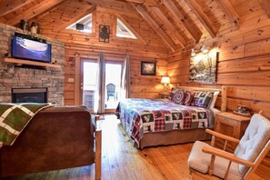 A cozy log cabin bedroom with a bed, a chair, a fireplace, and a television on the wall.