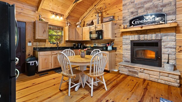 A wooden cabin interior with a stone fireplace, wooden dining table, and chairs.