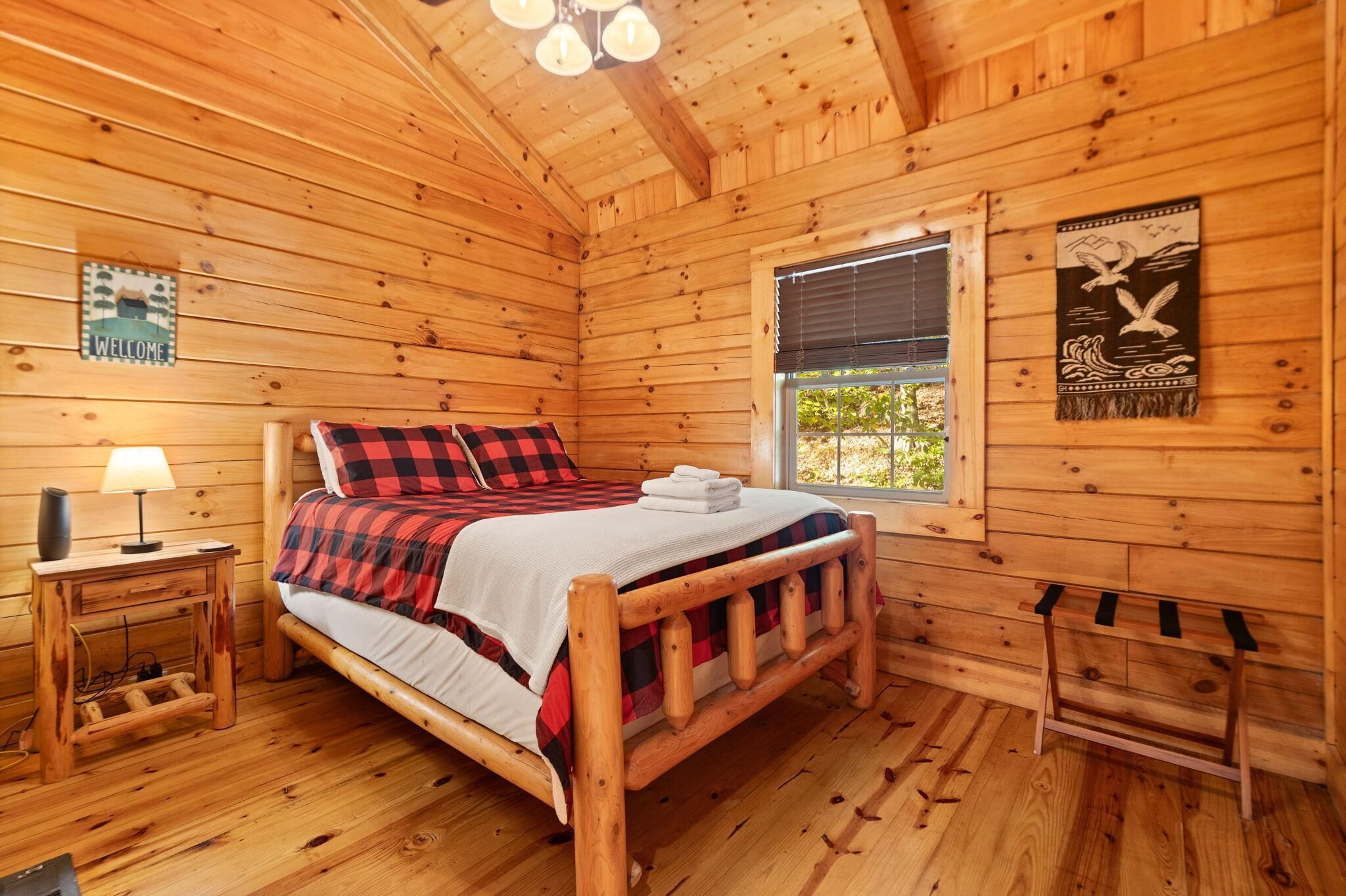 Une chambre dans un chalet en bois, avec un lit, une table de chevet, une fenêtre et une pancarte de bienvenue.