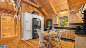 A wooden cabin interior with a kitchen featuring white cabinets, a refrigerator, and a dining table with chairs.