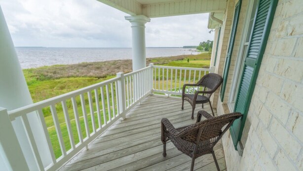 A wooden porch with white railings and two wicker chairs. - Dock House Guest Suite (Belhaven)