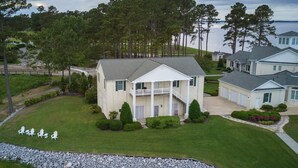 A two-story house with a covered porch, surrounded by a stone retaining wall and well-maintained lawn. - Dock House Guest Suite (Belhaven)