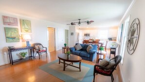 A spacious living room with a blue sofa, a coffee table, and a dining area in the background. - Dock House Guest Suite (Belhaven)