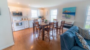 A modern kitchen with white cabinets, a dining table with chairs, and a blue couch in the living area. - Dock House Guest Suite (Belhaven)