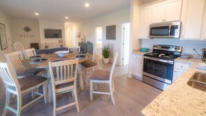 A modern kitchen with white cabinets, stainless steel appliances, and a dining area with wooden chairs and a table. - Flowers Landing Guest House (2 Suites) (Belhaven)