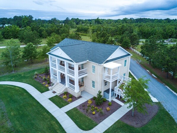 Stunning two-story home with a central entrance, flanked by balconies, set amidst a beautifully manicured lawn and lush greenery.