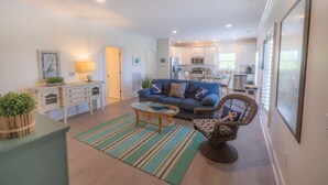 A modern living room with a blue sofa, a wicker chair, and a kitchen in the background.
