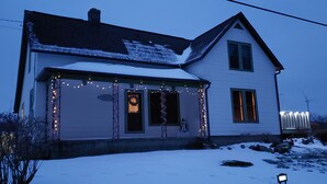 Une maison à deux étages, dont le toit est recouvert de neige et dont le porche est décoré de guirlandes lumineuses.