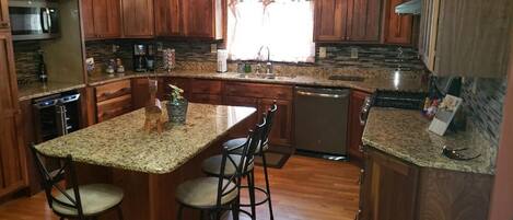 A kitchen with granite countertops, wooden cabinets, a central island with bar stools, and built-in appliances.