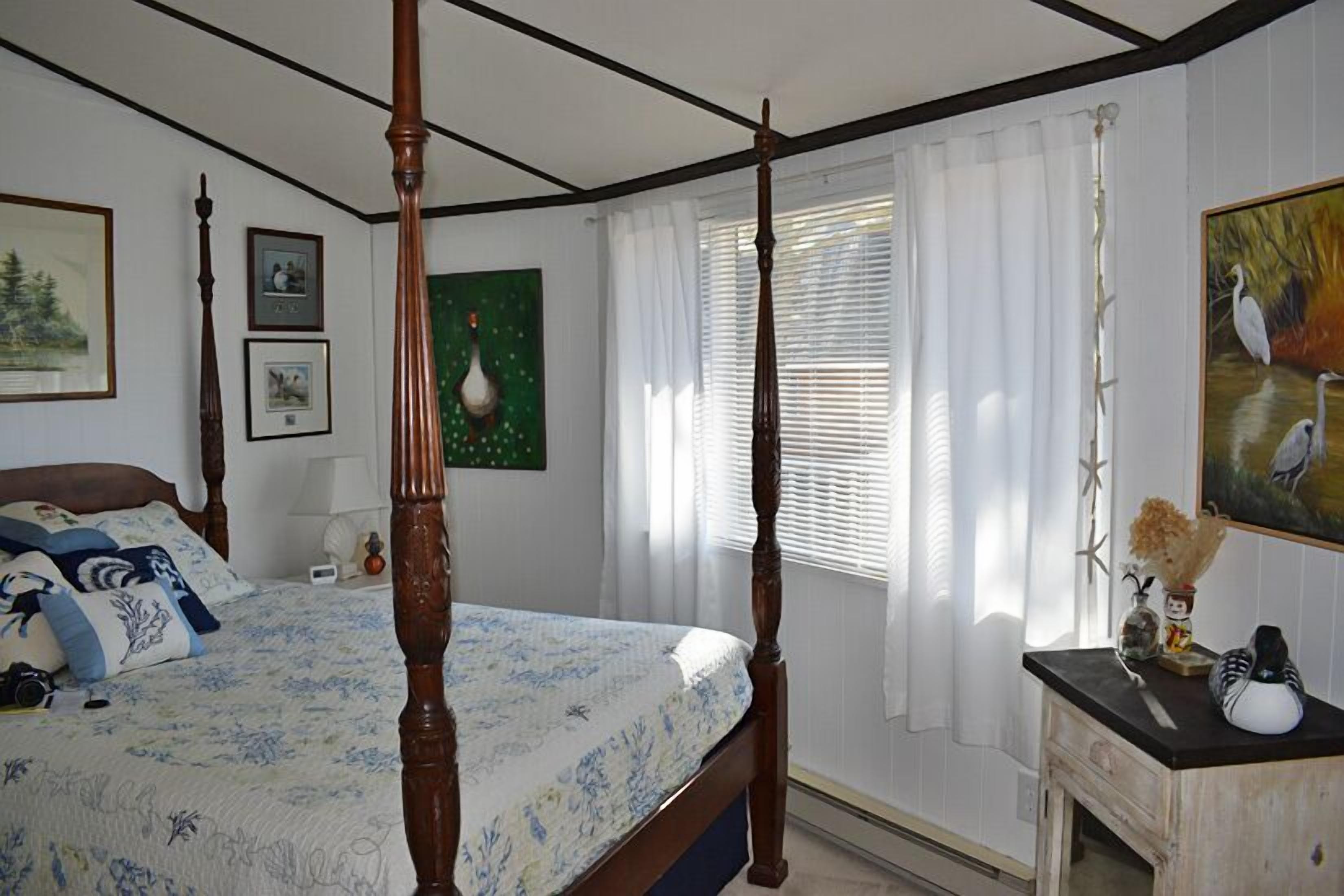 Une chambre à coucher avec un lit à baldaquin, une table de chevet, une commode et une fenêtre avec des stores.