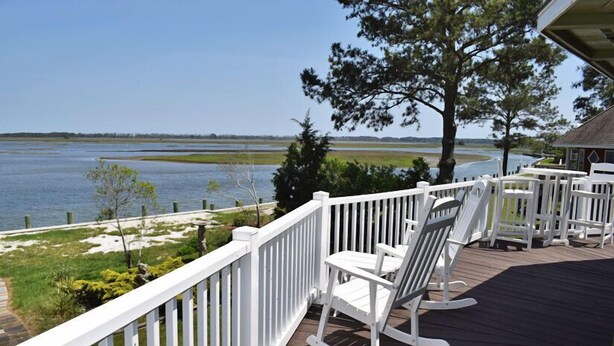 Une terrasse en bois avec des balustrades blanches, des fauteuils à bascule et une vue sur un lac.