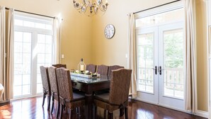 A dining room with a glass table, wicker chairs, a chandelier, and a clock on the wall. - Big Beautiful Georgian Bay Family Cottage (Tiny)