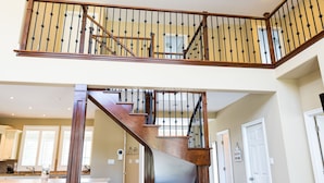 A spacious living area with a high ceiling, a wooden staircase with black balusters, and a kitchen in the background. - Big Beautiful Georgian Bay Family Cottage (Tiny)