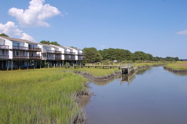 A waterfront hotel with multiple balconies and a dock extending into a calm river. - Fiddler Bay #6-End Unit Waterfront Townhome with Shared Crabbing Pier (Chincoteague)