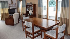 Un coin repas avec une table et des chaises en bois, un téléviseur, une bibliothèque et une fenêtre avec des rideaux.