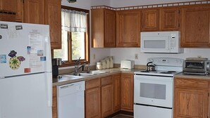 Une cuisine avec des meubles de rangement en bois, un réfrigérateur blanc, un four à micro-ondes, un grille-pain et un lave-vaisselle.