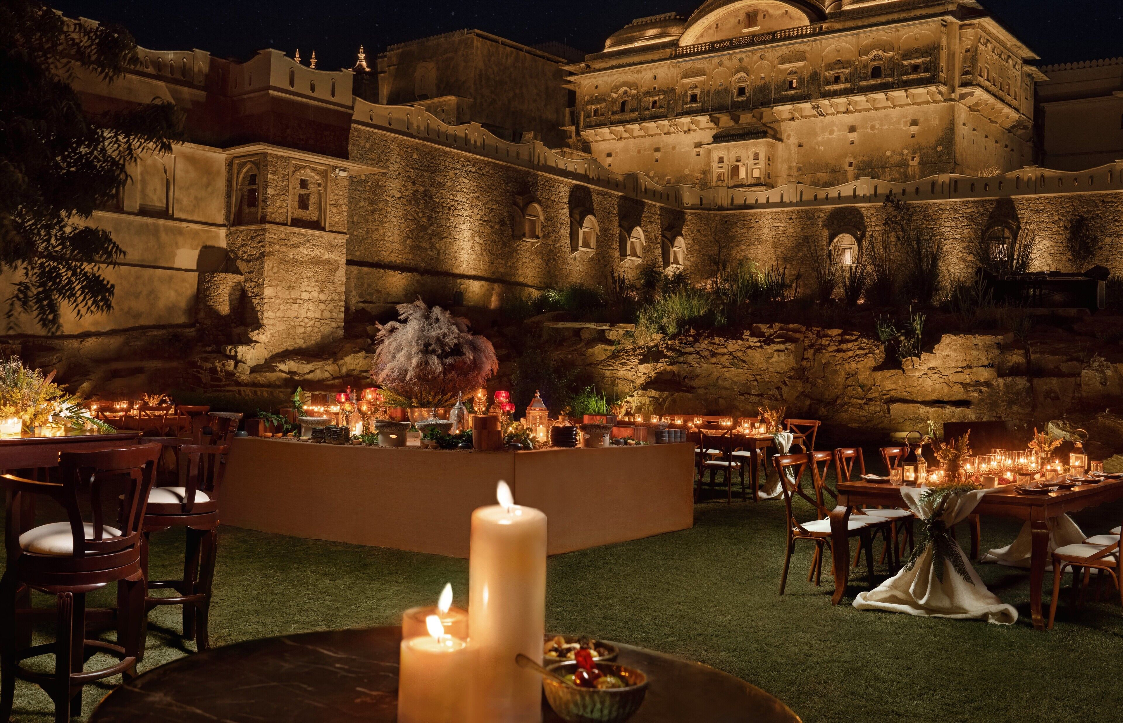 An outdoor dining area with tables and chairs, a large white candle centerpiece, and a historic building in the background.