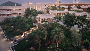 A large, historic building with multiple balconies and a central courtyard with palm trees and a water feature. - Six Senses Fort Barwara (Chauth Ka Barwara)