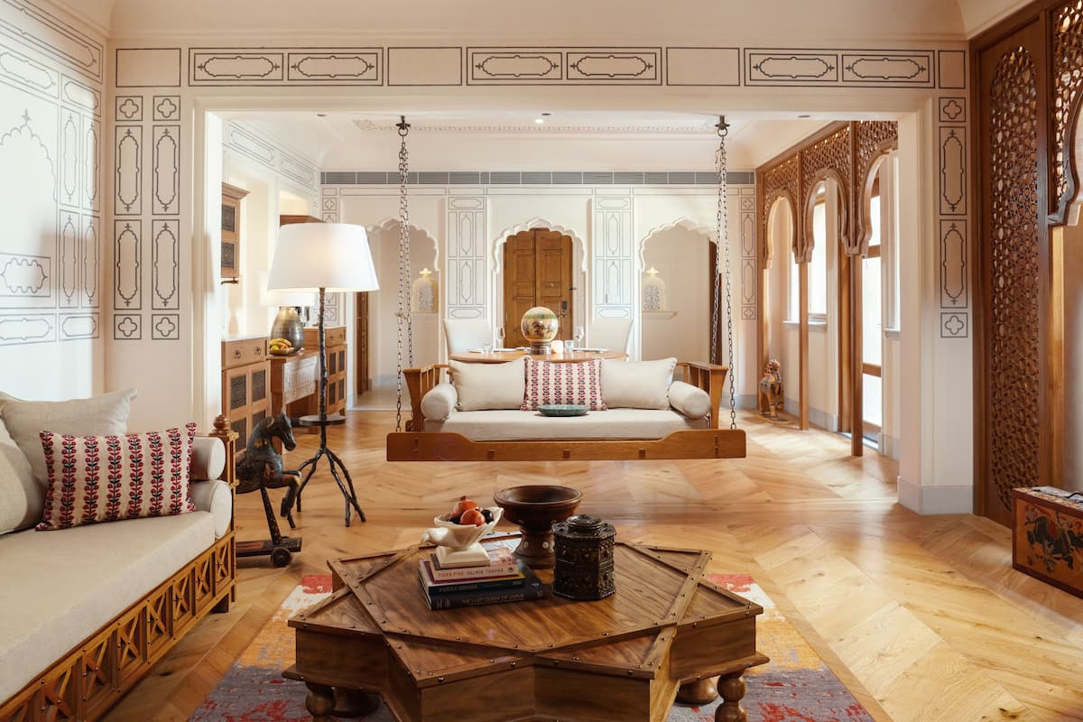 A spacious living room with a wooden floor, a swing, a sofa with patterned cushions, and a coffee table with books and decorative items.