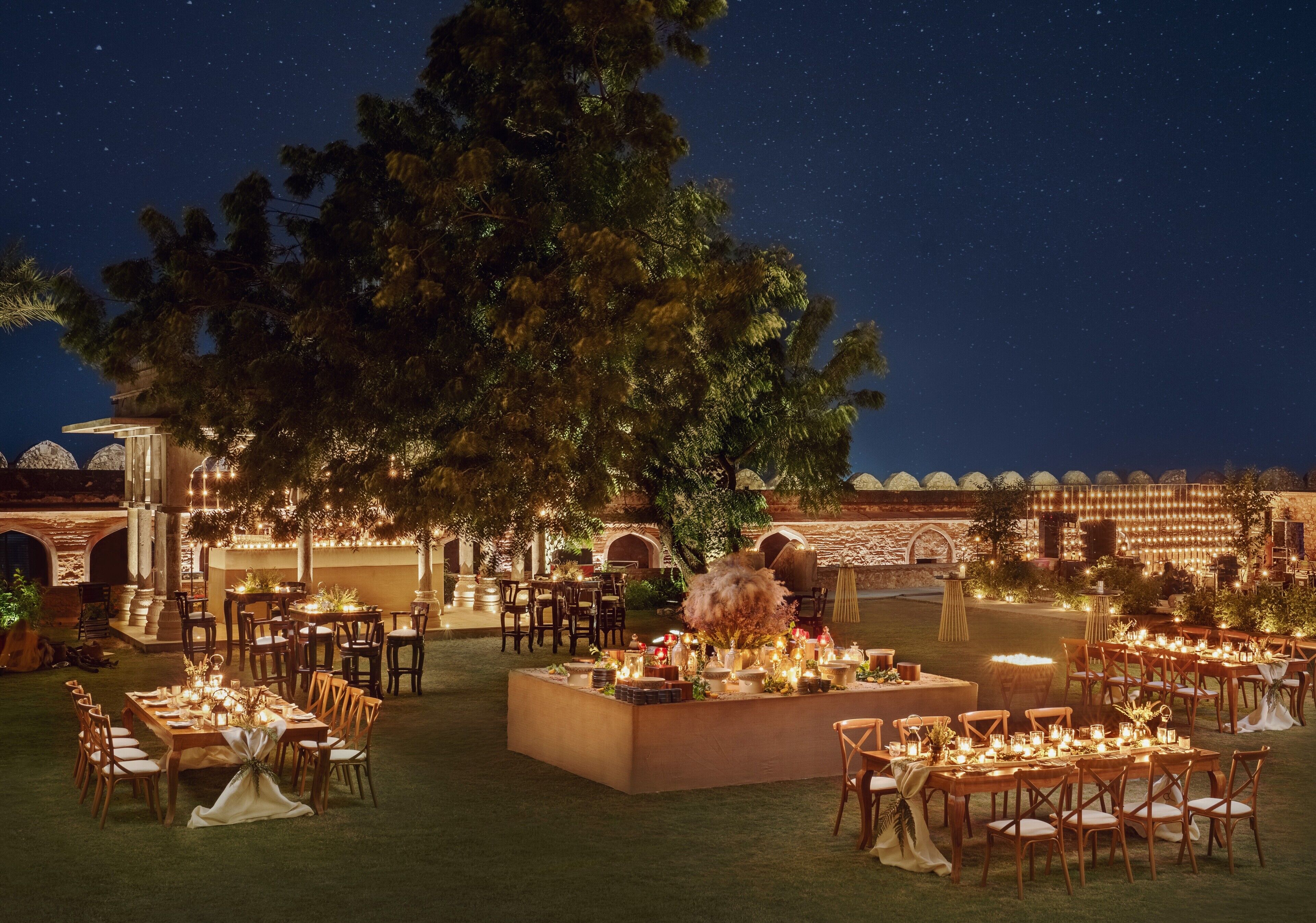 An outdoor dining area with tables and chairs, surrounded by trees and a night sky.