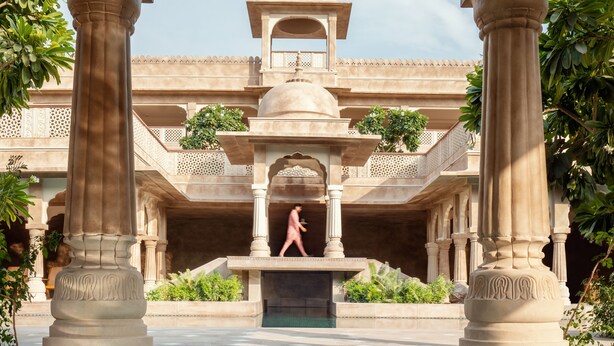 A pool area with a fountain, surrounded by ornate columns and a building with a dome in the background. - Six Senses Fort Barwara (Chauth Ka Barwara)