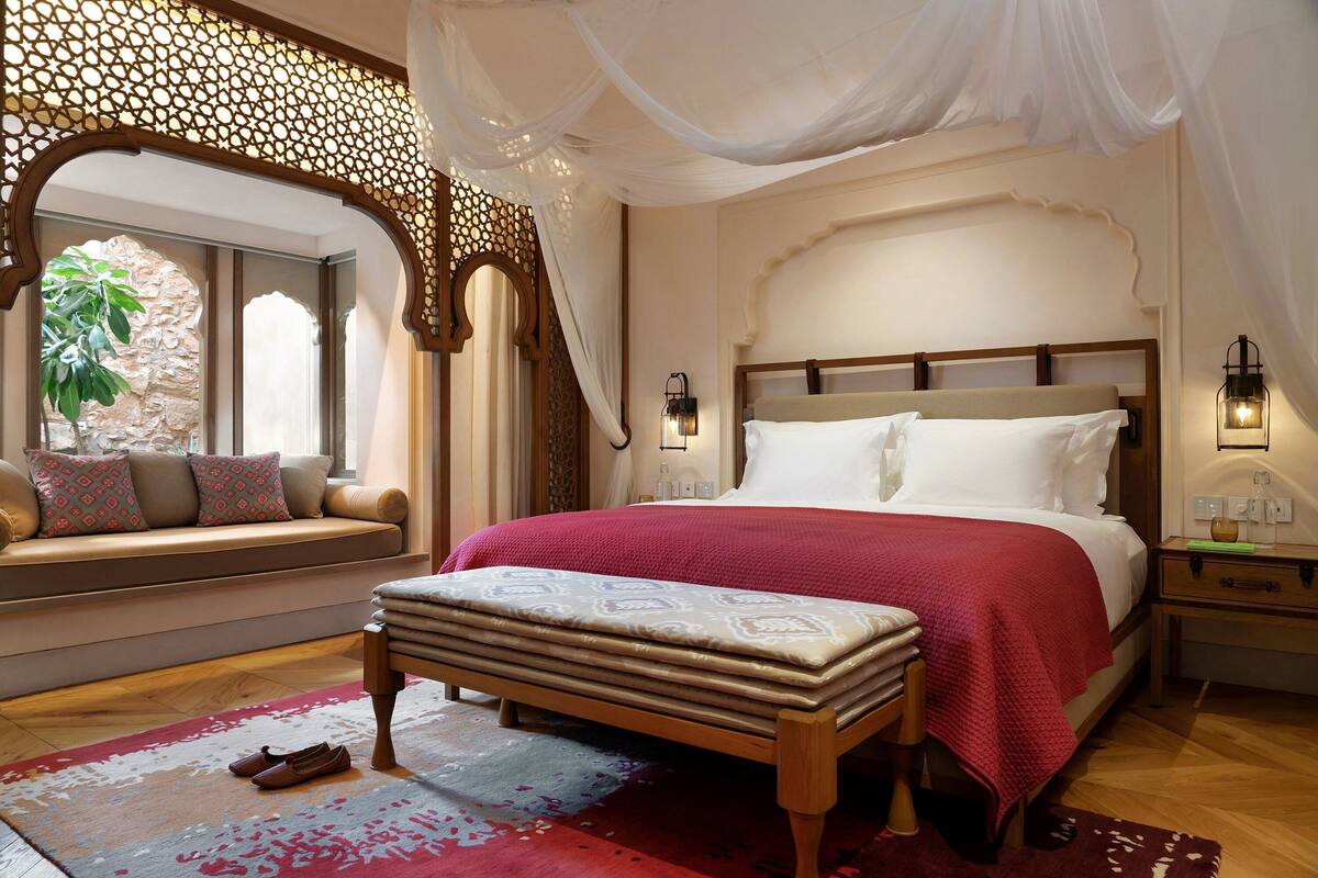 A bedroom with a large bed, a bench, a window seat, and a decorative wall.