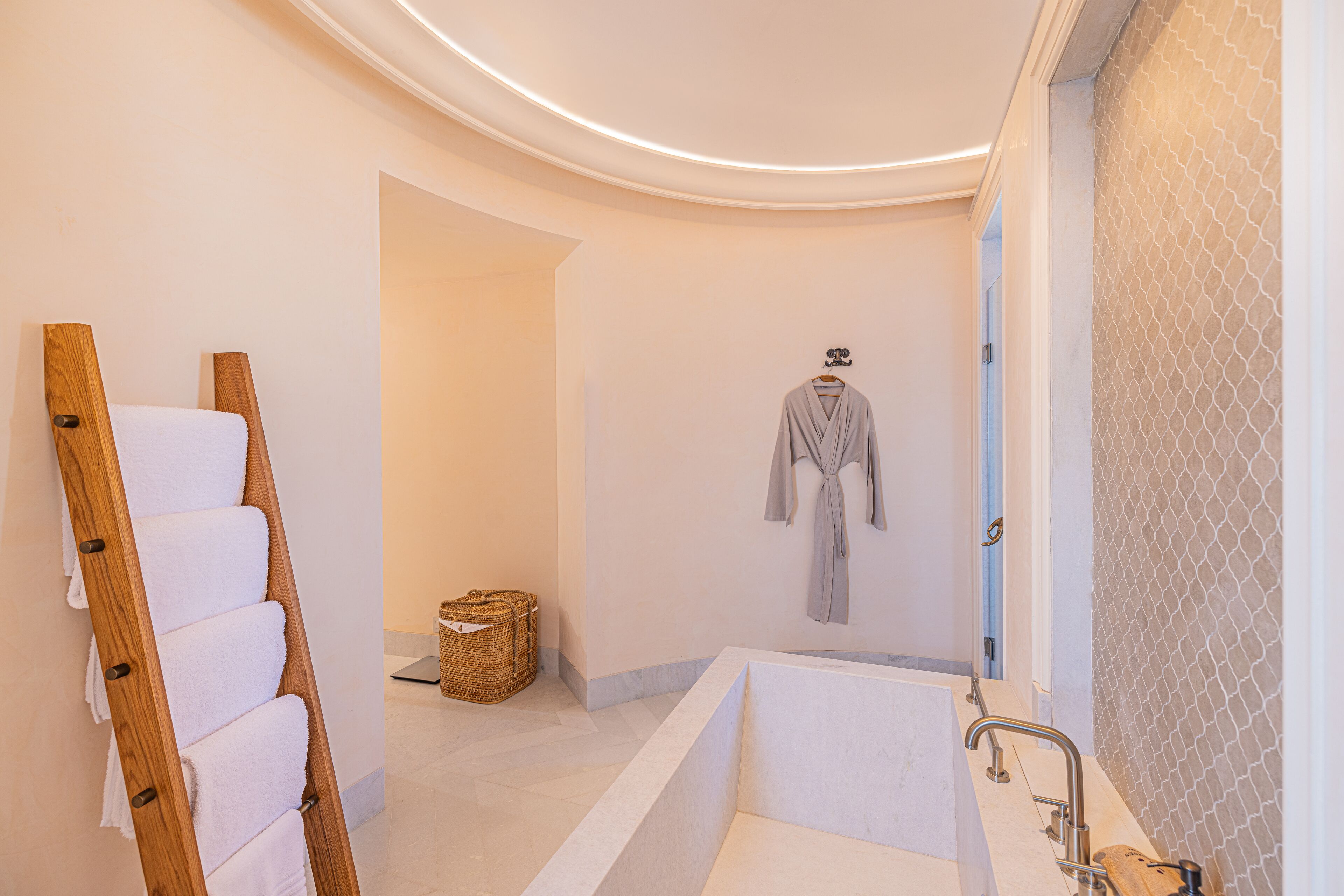 Un baño moderno con bañera, una escalera de madera con toallas y una bata colgada.