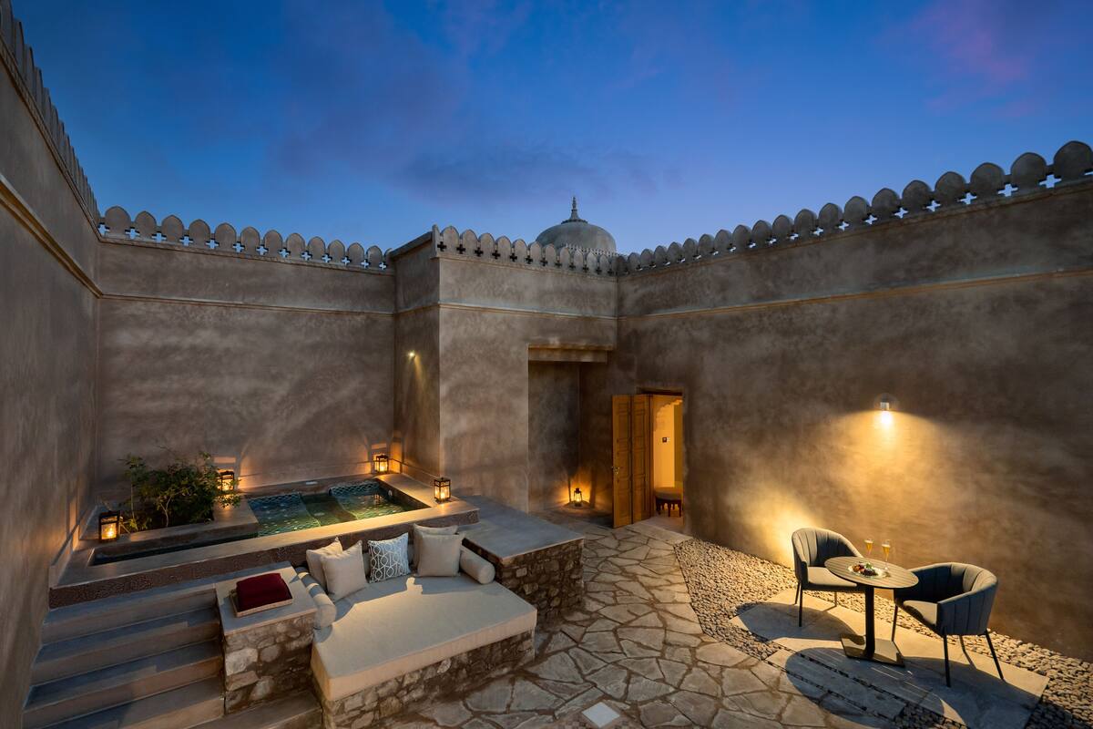 A serene outdoor seating area with stone steps, a small pool, and a dining table with chairs.