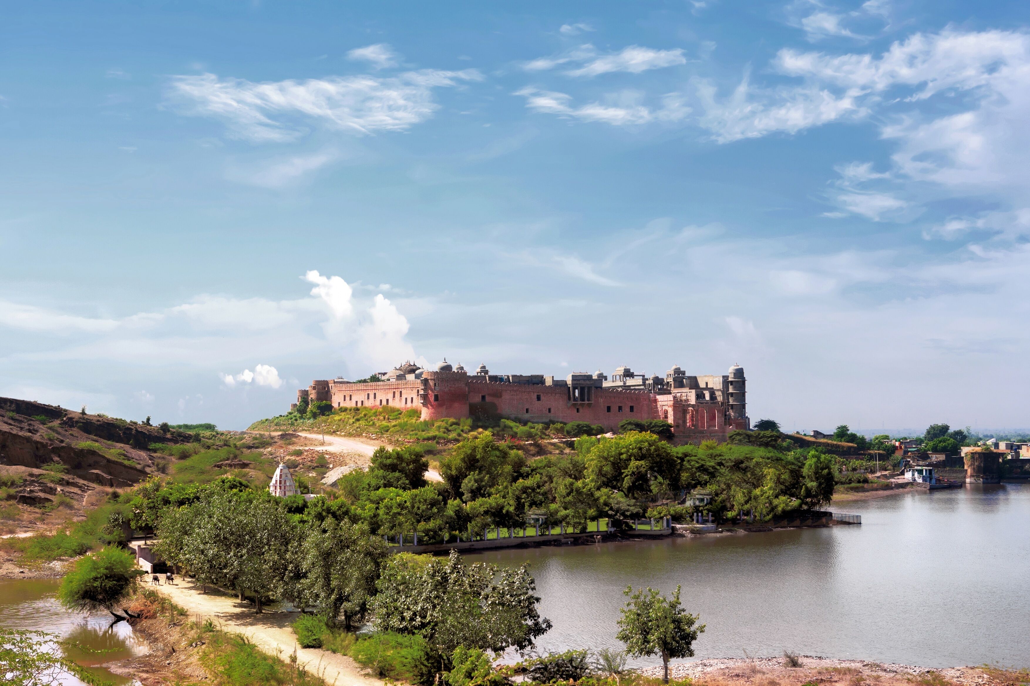 A historic fort on a hill overlooking a river, with a clear sky and lush greenery.