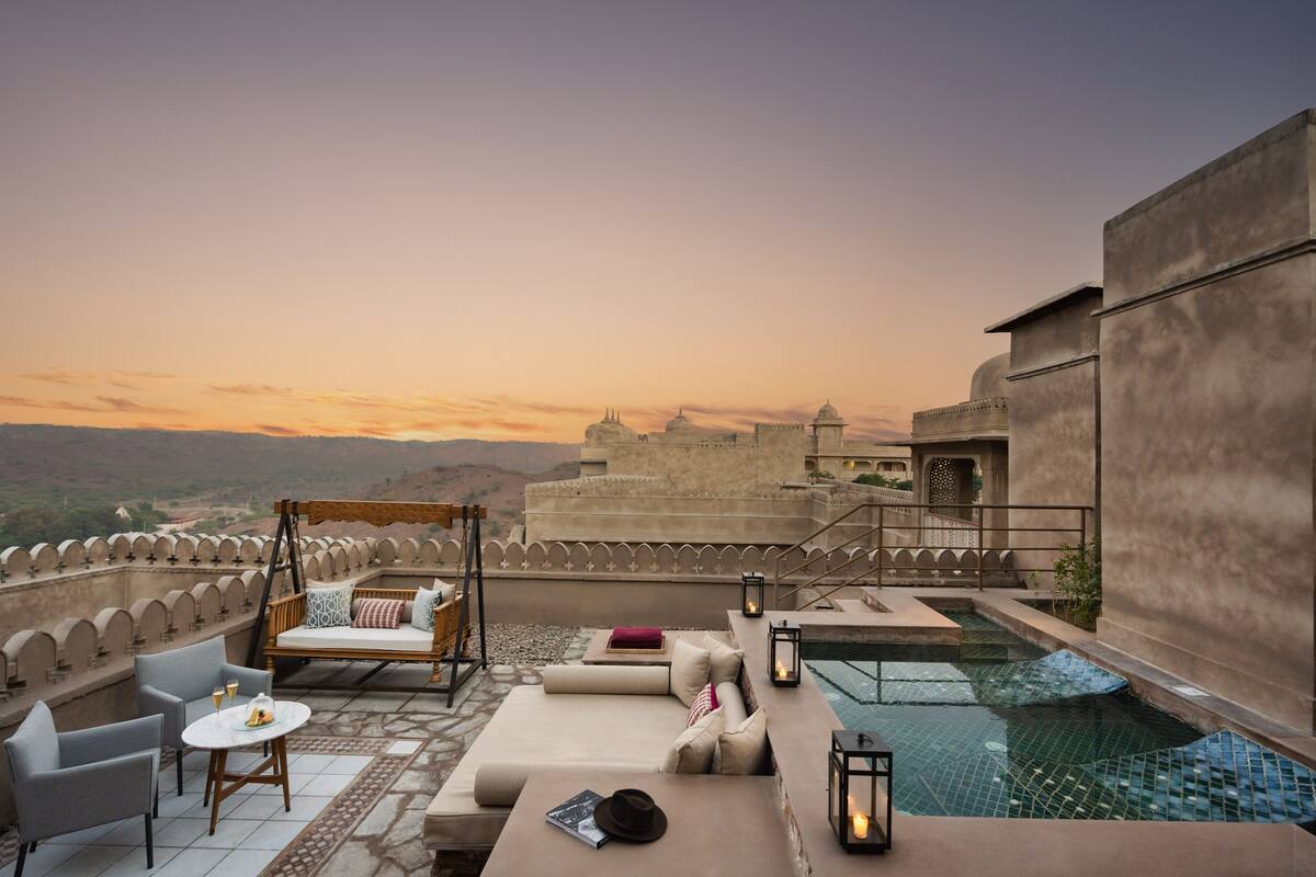 A rooftop terrace with a pool, seating area, and a view of a historic fort in the background.