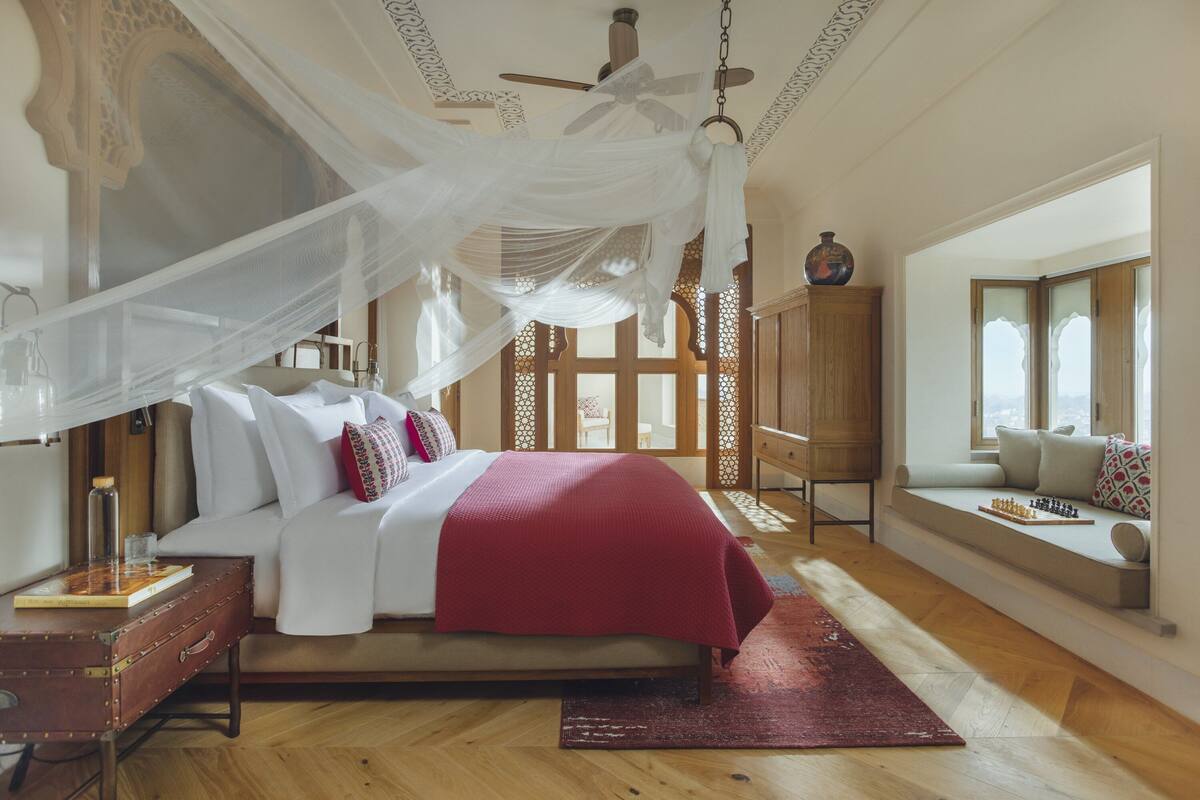 A bedroom with a bed, a nightstand, a wooden floor, a window seat, and a ceiling fan.