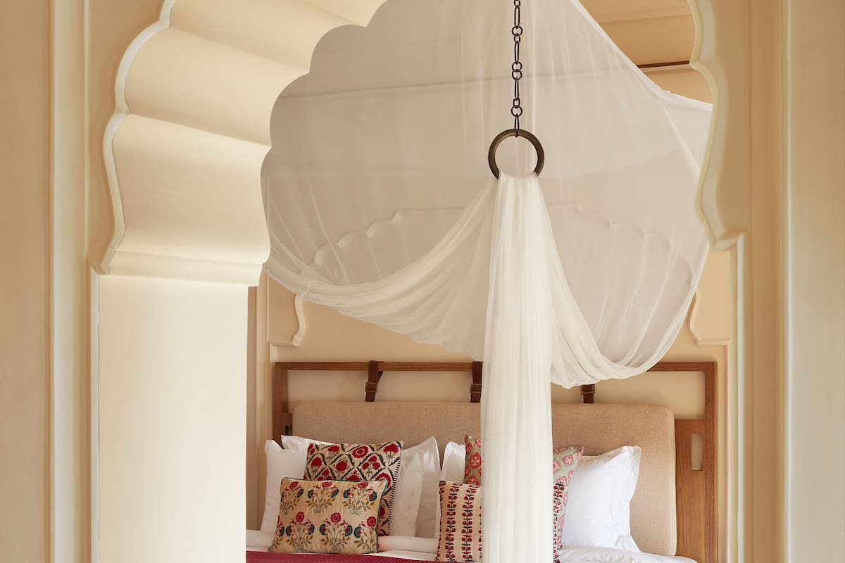 A bedroom with a canopy bed, a bench, and a red rug.