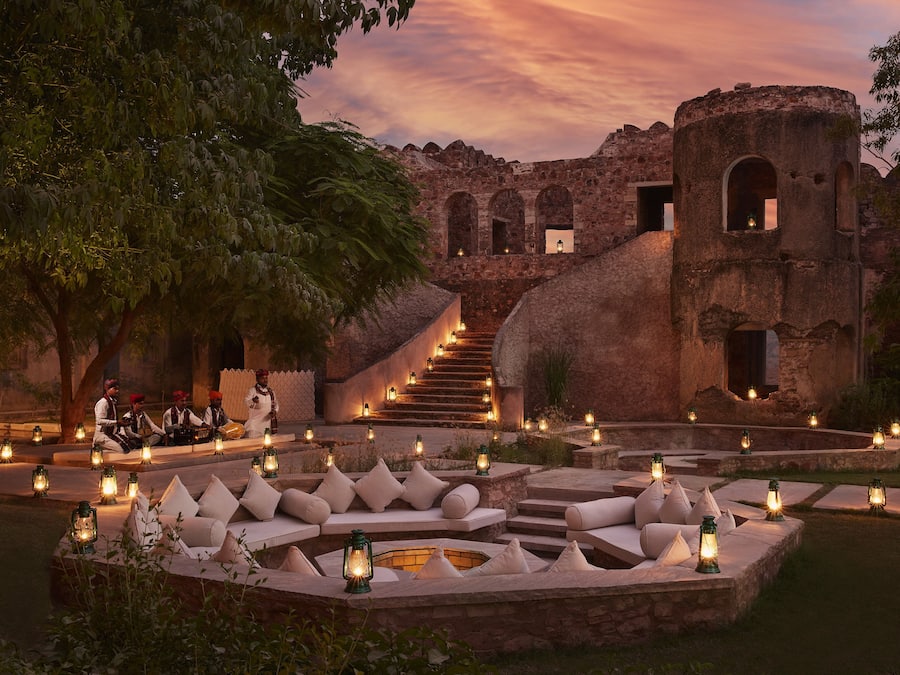 A courtyard with stone seating and lanterns, a staircase leading to a building, and a tree.