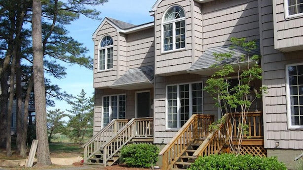 A two-story house with a wooden deck and a staircase leading to the front door. - Fowling View | Townhouse w/ Pier, Crabbing Dock & Sunset Views (Chincoteague)