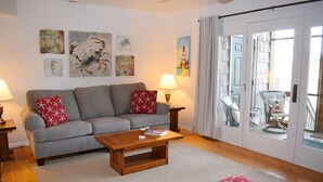 A living room with a grey sofa, red patterned cushions, a wooden coffee table, and wall art depicting sea creatures. - Fowling View | Townhouse w/ Pier, Crabbing Dock & Sunset Views (Chincoteague)