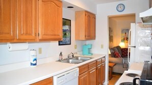 A compact kitchen with wooden cabinets, a dishwasher, a sink, and a stove. - Fowling View | Townhouse w/ Pier, Crabbing Dock & Sunset Views (Chincoteague)