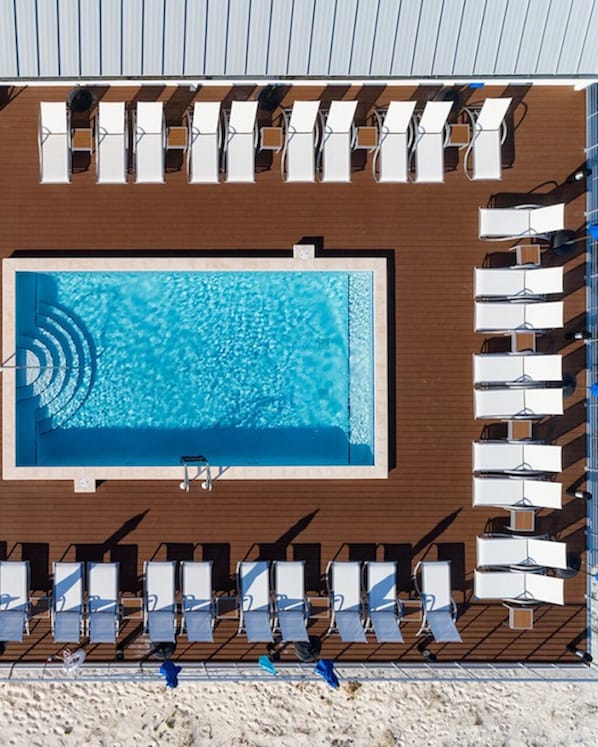 Une piscine sur le toit, dotée d’une terrasse en bois, entourée de rangées de chaises longues blanches et de parasols.